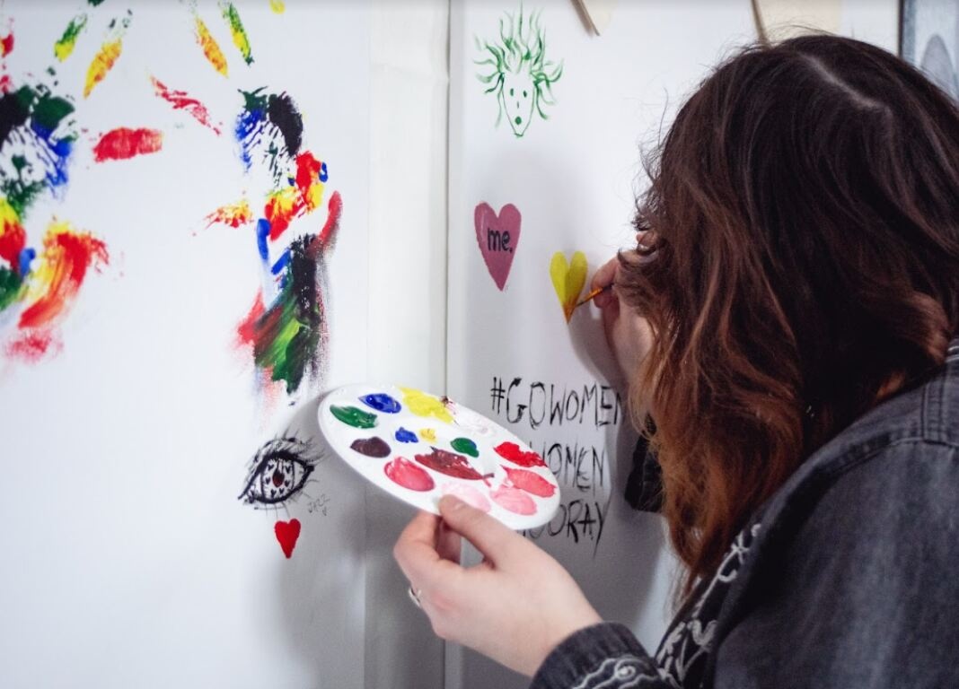 woman holds paint palette and paints on a wall